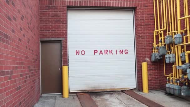 黄色い管が付いている煉瓦の壁およびガス メートルの金属の茶色のドアの隣の白いガレージのテキストを書く駐車場無し — ストック動画