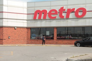 Metro bakkal zinciri ön tarafta, üzerinde logosu olan yaya müşterilerle yürüyor.