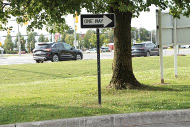 Tek yön beyaz ve siyah yatay dikdörtgen ok sağ işaret levhası ağacın altında, cadde arkası işaret okuyla aynı yöne giden iki araç var.