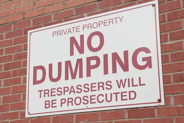private property no dumping trespassers will be prosecuted horizontal rectangle sign on brick wall, red white, close up
