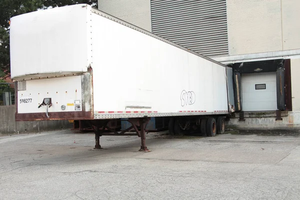two receiving bay garage doors next to each other in summer with one closed and the other with a large stationed parked white truck trailer storage in it, shot on angle