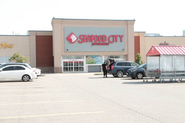 Deniz ürünleri şehri süpermarketinin ön giriş logosu ve park yeri müşterisi arabanın bagajına giriyor, geniş açı.