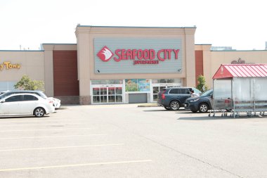 Deniz ürünleri şehri süpermarketinin ön giriş logosu ve park yeri. Müşteri aracıyla gidiyor. Geniş açı.