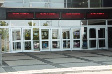 Dışarıdaki sinema salonunun girişinde üzerinde kırmızı renkli sinema panolarına hoş geldiniz yazan elektronik bir tabela var.