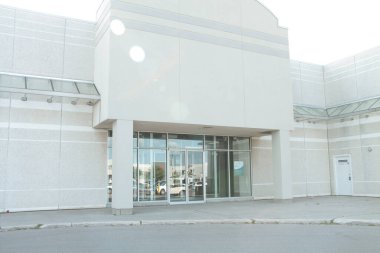 Boş jenerik boş mağaza önü bej bej bej beyazı. Tabela yok, altında sütunlar ve cam kapılar var. Park alanının yansıması.