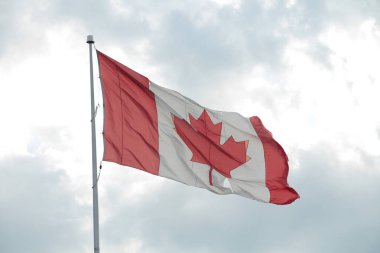 Büyük Kanada bayrağı bayrak direğinde dalgalanan rüzgarda dalgalanan yırtık bir delikle gökyüzü bulutları ardında parlayan güneş