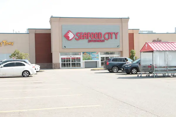 Deniz ürünleri şehri süpermarketinin ön giriş logosu ve park yeri. Müşteri aracıyla gidiyor. Geniş açı.