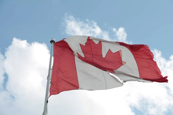 large canadian canada flag on flagpole with rip hole in it blowing waving in wind shot from underneath with sky clouds behind