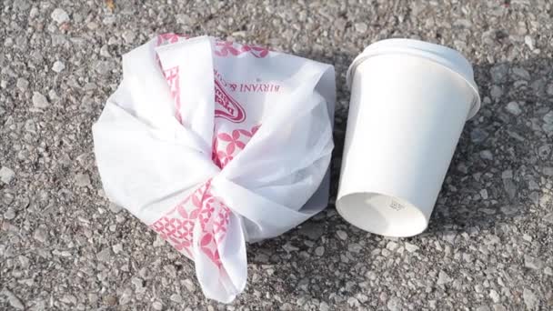 空的白色咖啡杯 盖在捆绑的塑料袋上 圆形早餐垃圾 铺在阳光灿烂的水泥混凝土路面上 — 图库视频影像