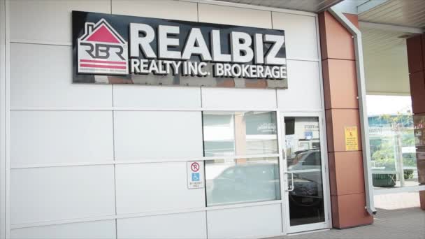 Realbiz房地产经纪公司独立拥有和经营的店面 橱窗入口门上方的正面有水平矩形标志 并有车辆通过的倒影 — 图库视频影像