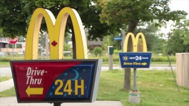 McDonalds yazları girişteki yazlık levhalarda, birbirinin önünde araçlar arka planda caddeden geçerken diğerinin çıkışında ise kapatılıyor.