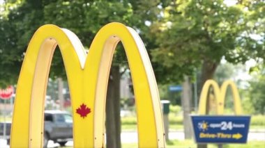 McDonalds yazları girişteki levhalarda bir diğerinin önünde araba trafiği geçen ve patlayan araçlarla birlikte soldaki logo çerçevesine yakın bir şekilde ilerler.
