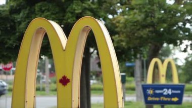 McDonalds yazları girişteki direklerde, biri diğerinin önünde araba trafiği arka planda caddeden geçerken, soldaki logo çerçevesinde kapanıyor.