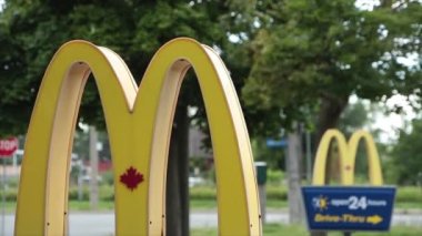 McDonalds yazları girişteki direklerde bir diğerinin önünde, rüzgarda esen ağaçla birlikte soldaki logo çerçevesine yaklaş.