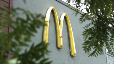 McDonalds 'ın kemeri sarı yay. Logo restoran duvarında. Dışarıdaki duvarda, parlak yaz gününde yapraklar ön planda uçuşuyor.