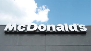 McDonalds gri restoran binasının duvarına beyaz harflerle işaret logosu yazıyor. Dışarıdaki orta çerçevenin arkasına bakan bulutlar hareket ediyor.