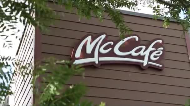 木の枝が付いているレストランの建物の茶色の壁の側面のMccafeのMcdonaldのロゴは外の表面を覆う前景で積極的に吹きます — ストック動画