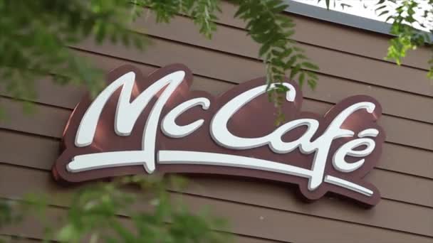 Mccafe マクドナルドのロゴ レストランの建物の側面の茶色の壁 木の枝の葉は外の表面を覆う前景で吹いています 閉じます — ストック動画