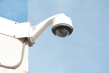 Geniş açılı güvenlik kamerası yaz günü duvarın köşesine monte edilmiş, arkasında mavi gökyüzü, beyaz ve siyah, kapatın.