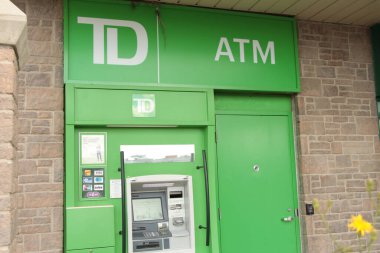 Toronto Dominion Green Bank ATM 'si. Logosu dışarıda. Yazın dışarıda, bej tuğlalı duvarın yanında.