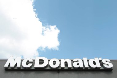 McDonalds altyazı işareti logosunu gri restoran duvarına beyaz olarak yazıyor. Arkasında bulutlar var.
