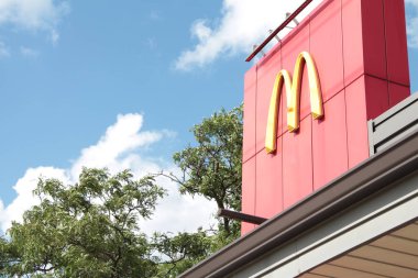McDonalds 'ın kemer yayı sarı logosu restoranın tepesinde kırmızı duvar örüyor ve yaz günü ağaç bulutları gökyüzünde.