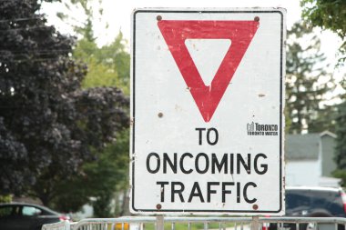 Yaklaşan trafik dikdörtgeninin verim sembolü. Arkasında ağaçlar olan metal çitin üzerindeki beyaz kırmızı işaret.