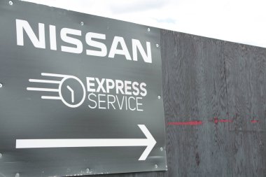 Nissan ekspres servis alanı siyah beyaz tabelası saat resmi çizimi ve ok dışarıdaki siyah tahta duvara vidalanmış.