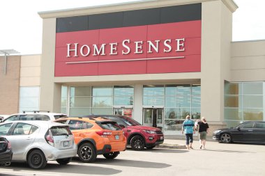 İki müşterinin olduğu park yerinin önünde Homesense mağazası girişi. İnsanlar mağazaya doğru yürüyor.