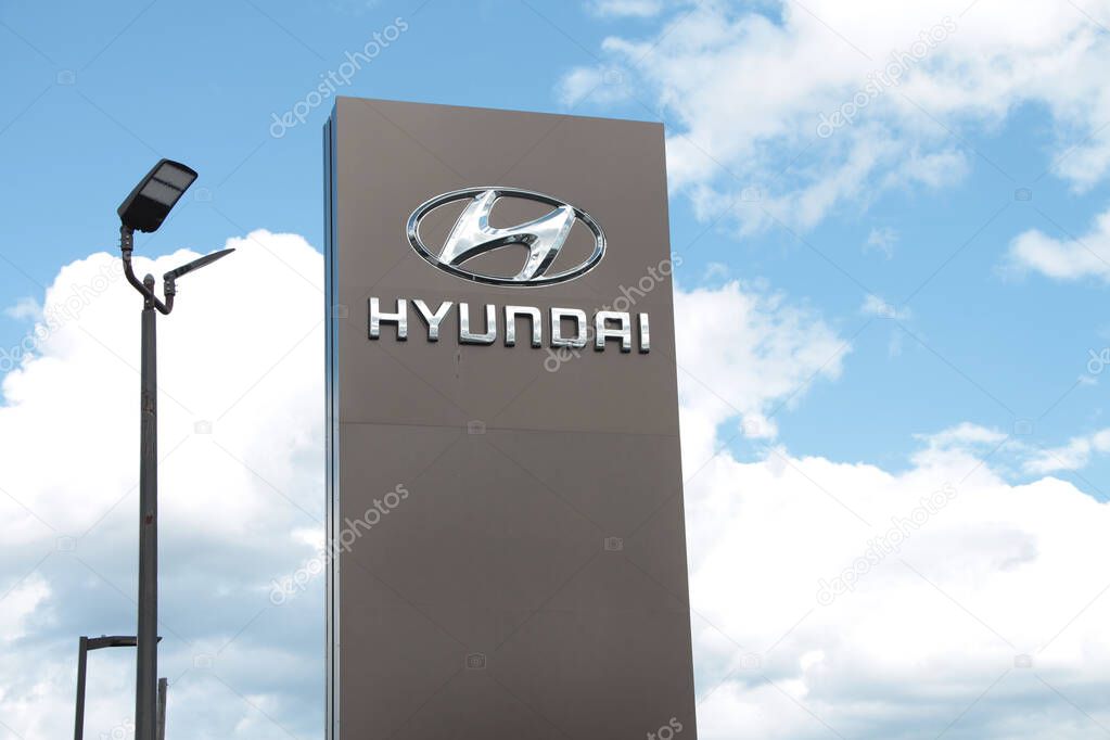 Hyundai silver logo sign on gray pillar outside outdoors exterior with clouds sky behind next to light post