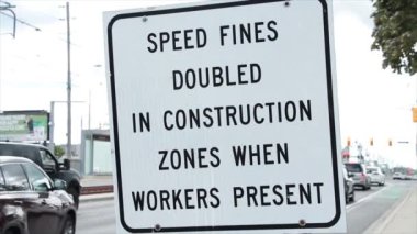 İnşaat bölgelerinde hız cezaları iki katına çıktı. İşçiler kare beyaz işaret levhasında yazı yazarken araç trafiği arkada hareket ederken araç trafiği ile başlık metni kullanıldı.