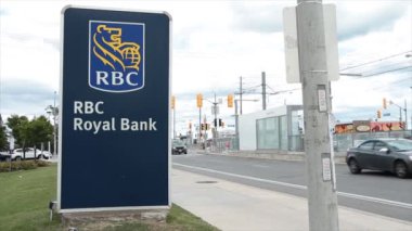 RBC Kanada kraliyet bankası dikey dikdörtgen işareti üzerinde çimenler üzerinde mavi işaret levhası kaldırım ve sokak yolunun yanında araç trafiği var.