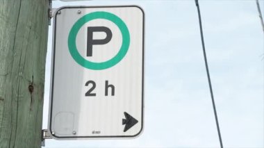 Park yerine 2 saat için izin verildi. Beyaz yeşil dikey dikdörtgen işareti, ok ve p ile yeşil daire şeklinde, ahşap direğin arkasında gökyüzü.