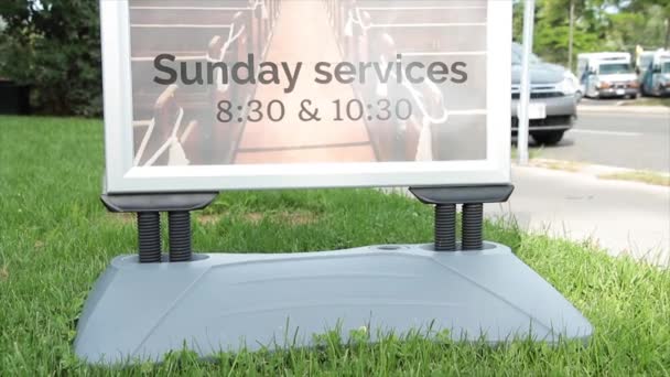 日曜日のサービス 830および1030 時間のサイン 道の隣に芝生のサイン情報 夏の明るい日に車の車が引き上げ 駐車場および交通および人渡る — ストック動画