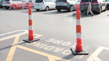 Yığınla uzun, turuncu, beyaz sütunlar yükleme sahasının tepesinde yazın otoparkta manşet metni yazarken market arabalarını iten ve geçen araçlarla birlikte.