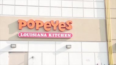 Popeyes Louisiana mutfağı. Restoranın arkasındaki duvarda turuncu beyaz işaret logosu. Altında iki ışık var.