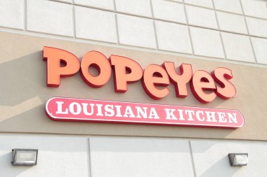 Popeyes Louisiana mutfak turuncu beyaz işaret logosu restoran binasının arkasındaki duvarda, altında iki ışık var, kapat.