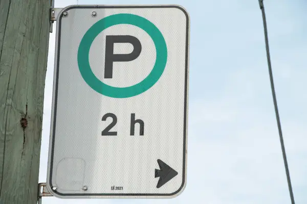 停车时间为2小时 车架左边为白色黑色竖直矩形标志 箭头和绿色圆圈在木柱上 后面为天空 — 图库照片