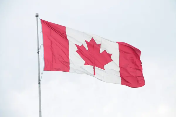 canada canadian flag blowing waving in wind on flagpole outside exterior with sky behind
