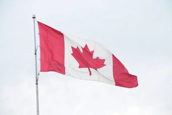 canada canadian flag blowing waving in wind on flagpole outside exterior with sky behind and top right of flag crinkled