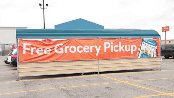 無料の食料品ピックアップサインバナー ショッピング食料品のカートの横に携帯電話のウォルマートのロゴ 駐車場の人車の車のキャノピー ホワイトオレンジ — ストック動画