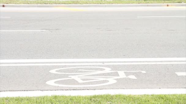 自転車自転車サイクリストレーン 道路の草の隣と道路上の白いペンキのイラストの自転車の絵とそれの重い交通機関車によって渡る車 — ストック動画