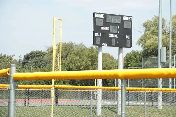 turned off baseball electronic digital scoreboard on posts in outfield with time home guest inning ball strike out with fence foul line in foreground