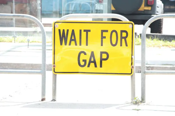 wait for gap writing caption text street road sign on island in middle of road in black on yellow
