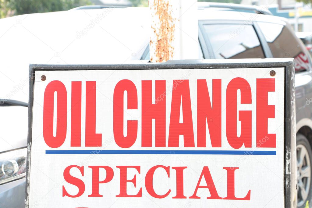 Oil change special sign writing caption text exterior outside in red on white on bright day with car vehicle behind