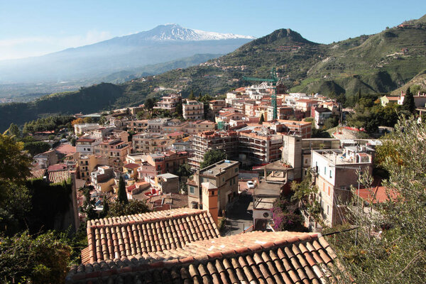 taormina sicily italy wide shot homes houses buildings on mountain with mount mt etna volcano in the background with snow on it