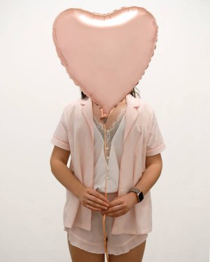 Pijamalı bir kadın kalp şeklinde pembe bir balon tutuyor.