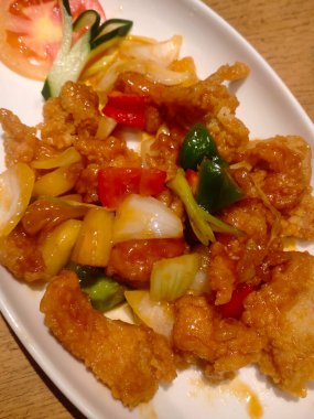 Beyaz bir tabakta servis edilen sebzelerle pişirilmiş tatlı ve ekşi un balığı, yakın görüş, seçici alan derinliği. Yemek menüsü fotoğrafları için kullanılabilir.