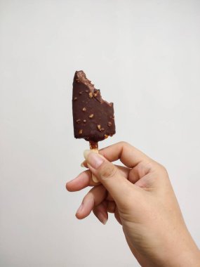 Isırılmış çikolatalı fıstıklı dondurma beyaz duvar arkasında el ele tutulur..