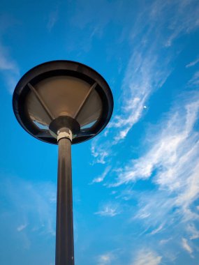 Işıksız bir bahçe direği mavi gökyüzü arka planına karşı Bulutlar ve ay eşliğinde.